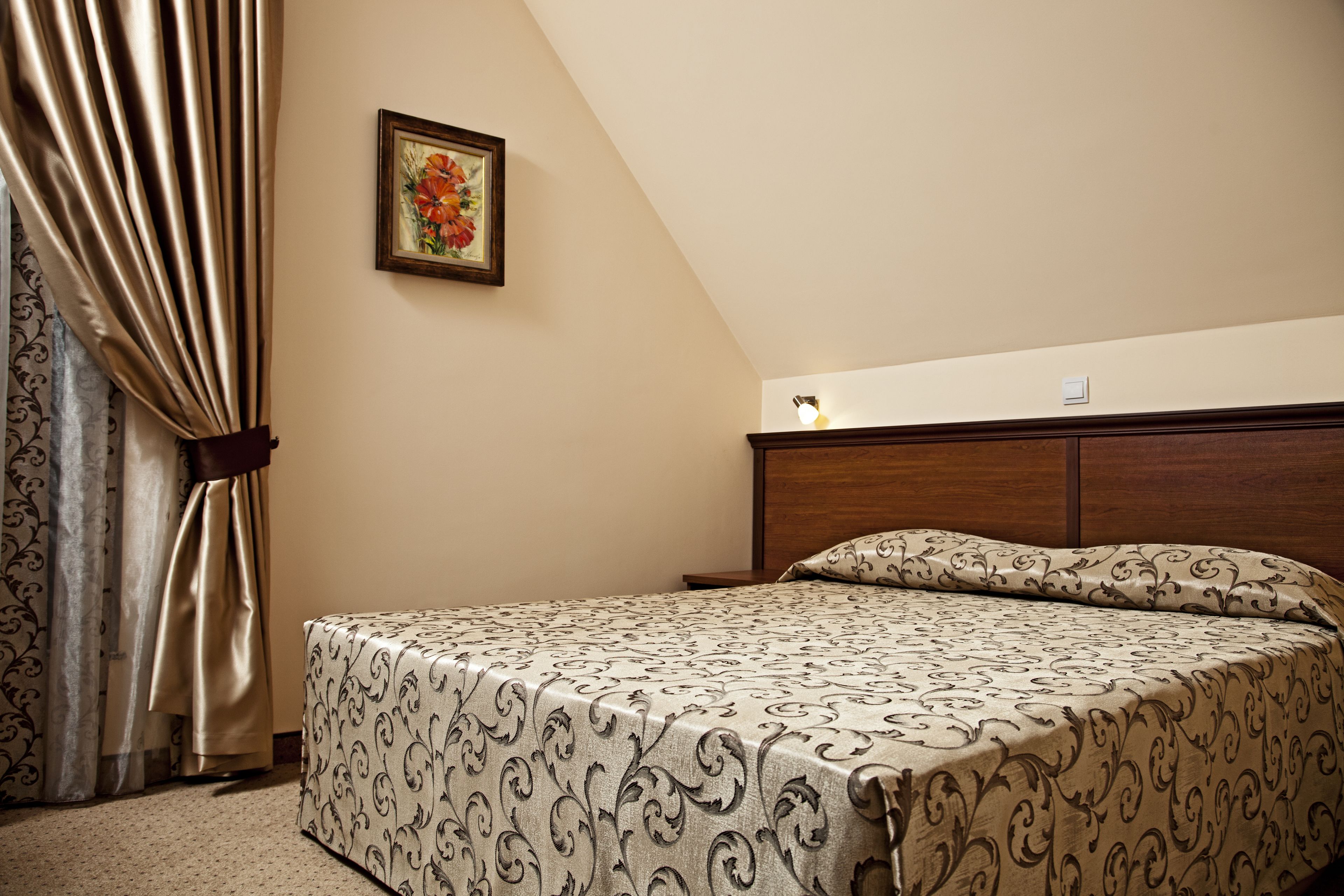 A bedroom with a bed, curtains, a framed picture, and a nightstand.