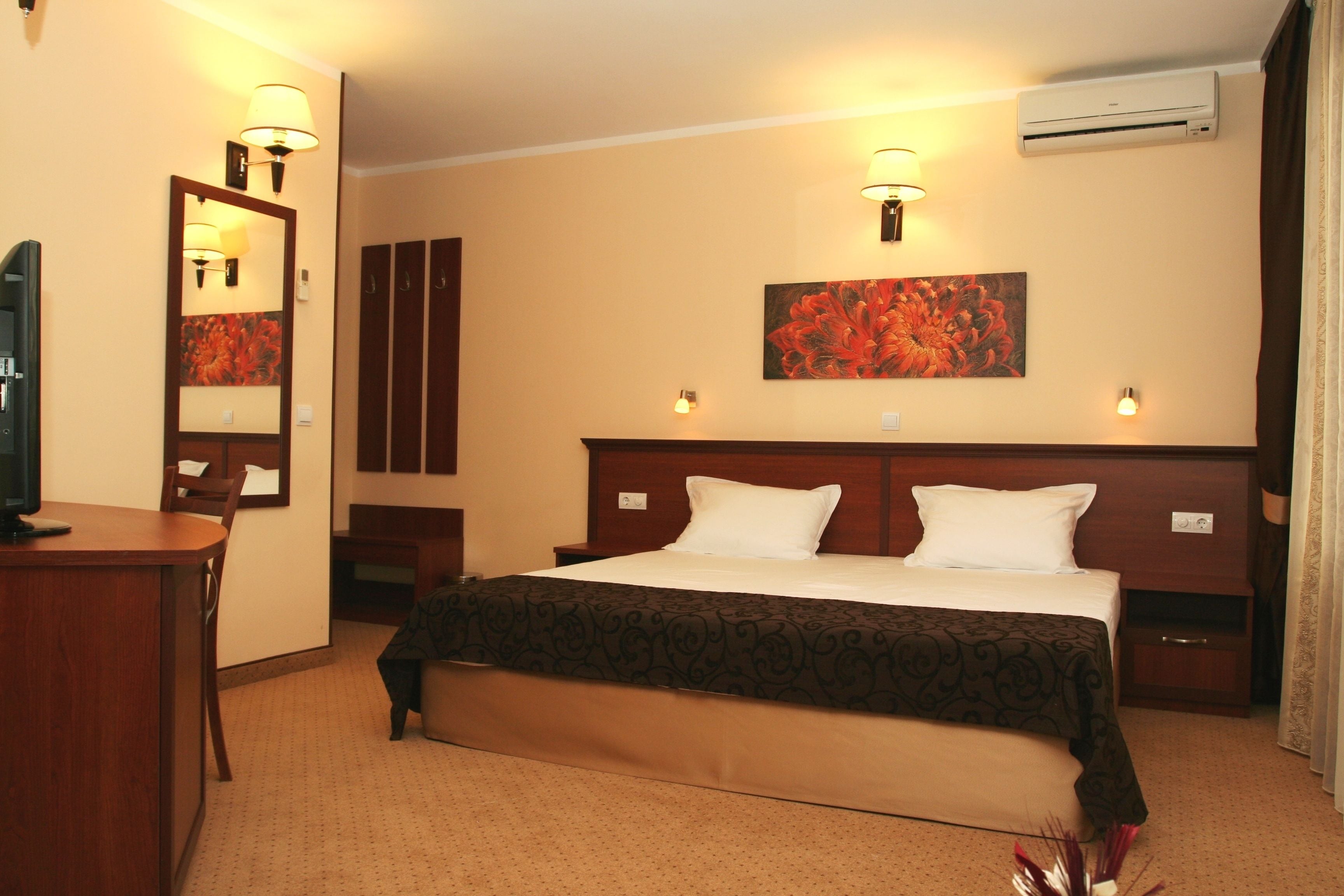 Una habitación de hotel con cama, mesitas de noche, escritorio, espejo y aire acondicionado.