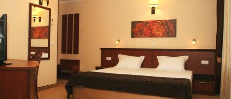 A hotel room with a bed, bedside tables, a desk, a mirror, and an air conditioning unit.