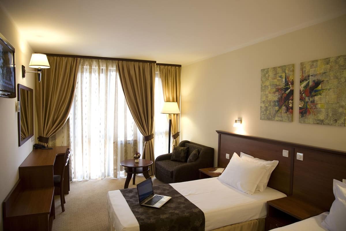 A hotel room with a bed, a desk, a chair, a sofa, a lamp, and artwork on the wall.