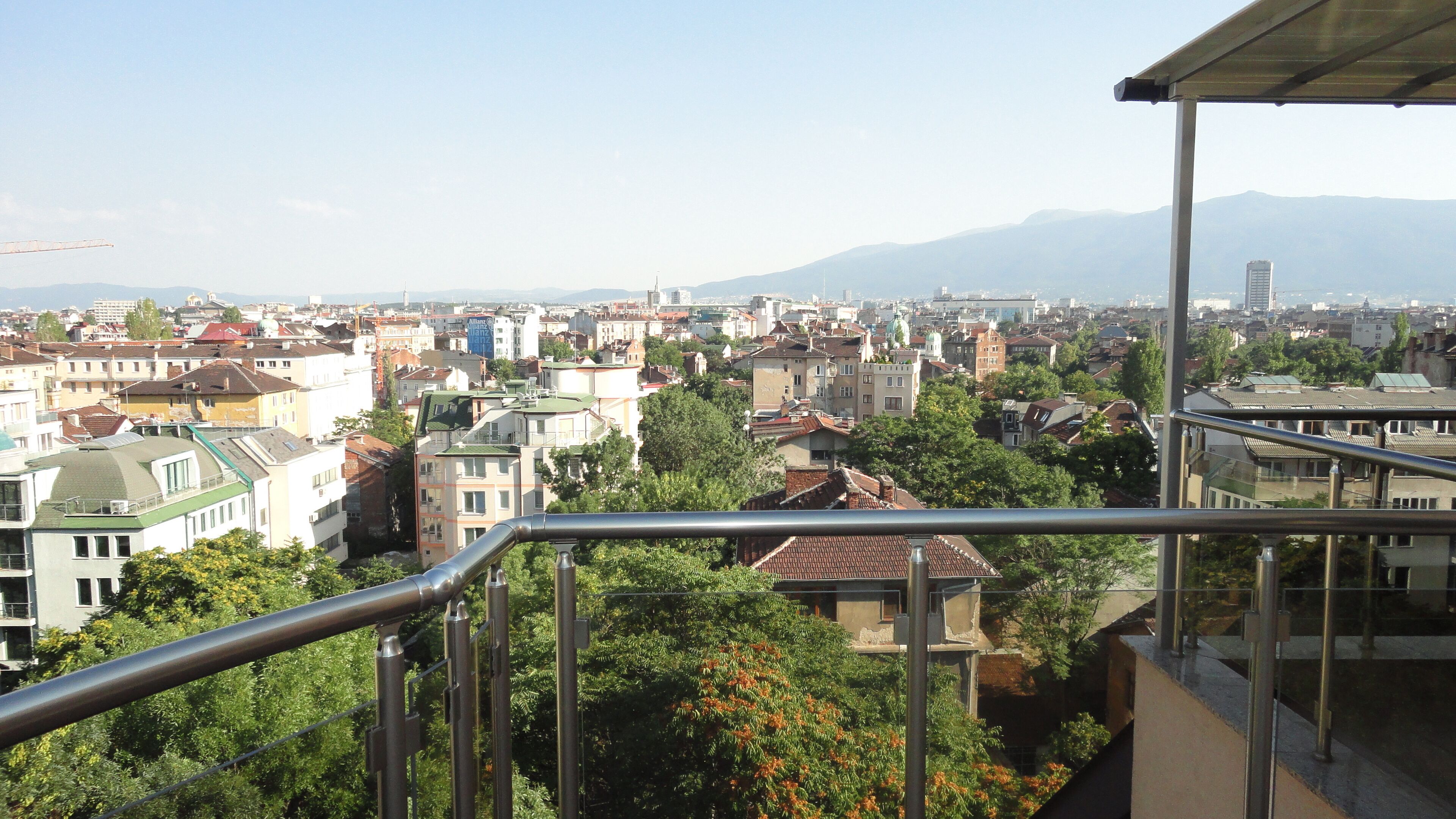 A cityscape with a mix of residential and commercial buildings, a prominent church with a green dome, and a mountain range in the background.
