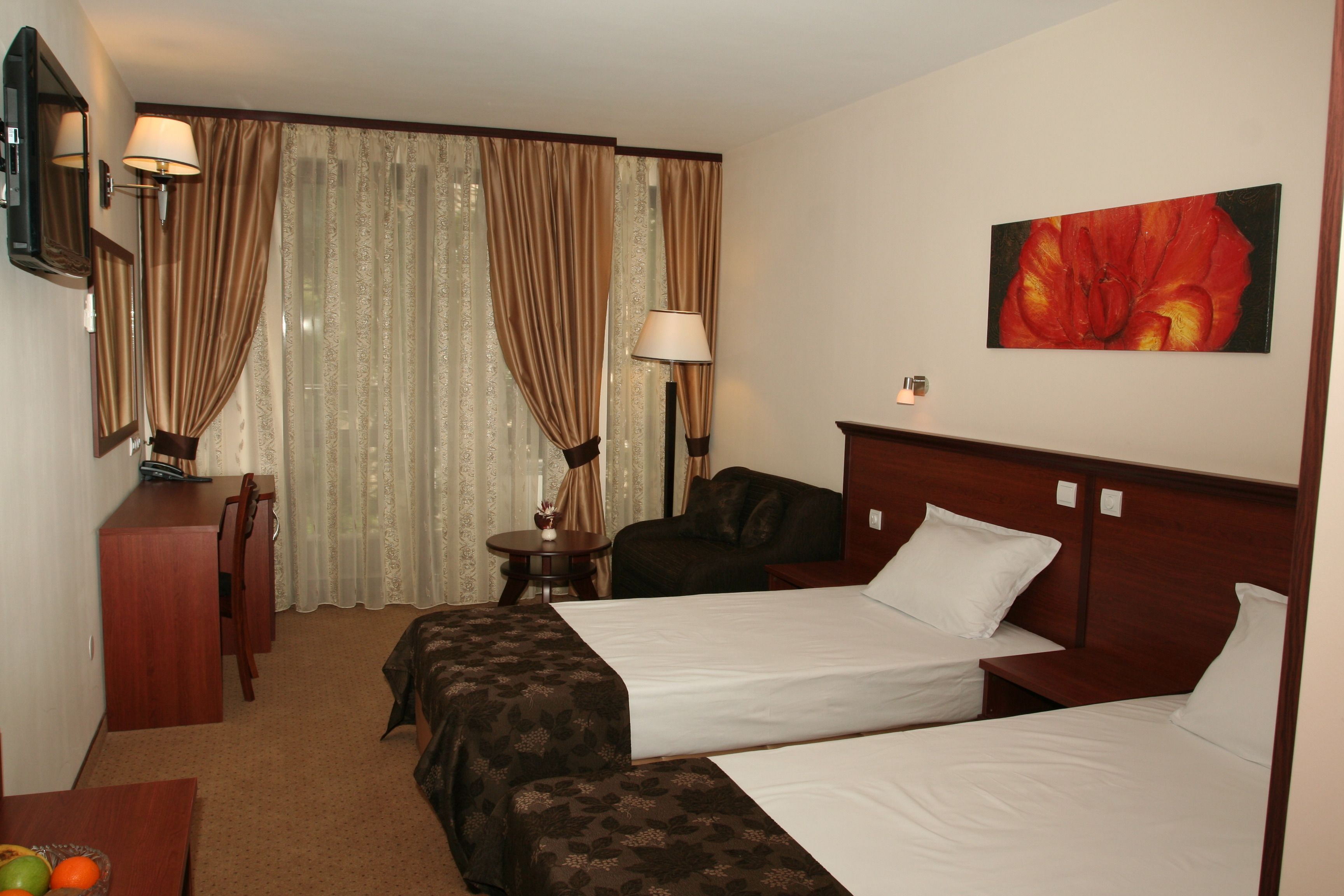 A hotel room with two beds, a desk, a chair, a lamp, and a painting on the wall.