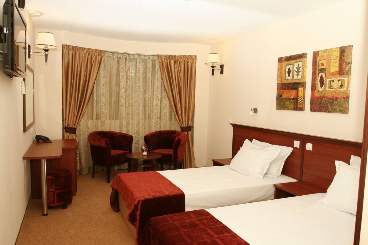 A hotel room with two beds, a desk, two chairs, a small table, and a TV.
