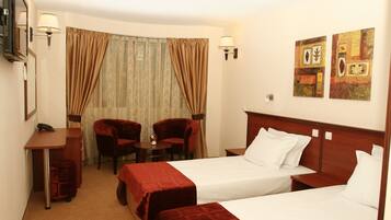 A hotel room with two beds, a desk, two chairs, a small table, and a TV.