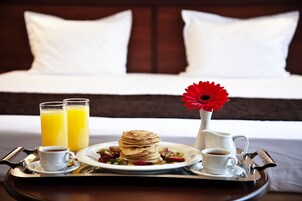 A breakfast tray with pancakes, juice, coffee, and a flower on a hotel room table.