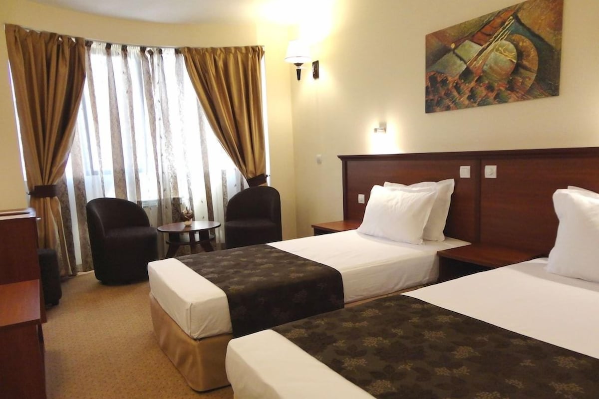 A hotel room with two beds, a desk, a chair, and a window with curtains.