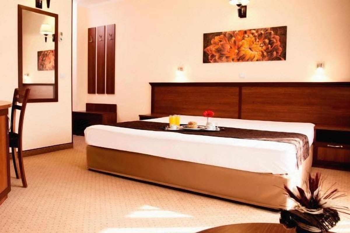A hotel room with a bed, a desk, a chair, and a small table with a tray.