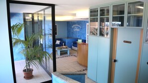 A hotel reception area with a blue wall, a reception desk, a blue sofa, and a potted plant. - Hotel Residence La Baia (Castelsardo)