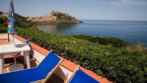 A seaside terrace with blue lounge chairs, a table, and a colorful umbrella. - Hotel Residence La Baia (Castelsardo)