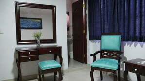A room with a wooden desk, two chairs, a mirror, and a painting on the wall.
