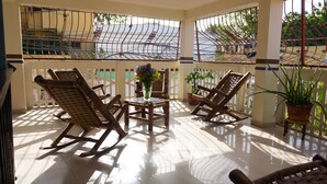 A sunlit patio with two rocking chairs, a small table with a vase of flowers, and potted plants.