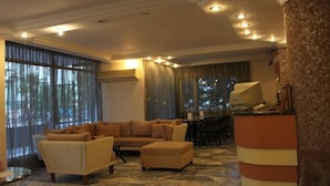 A spacious living room with a beige sofa, a matching ottoman, and a dining area with a long table. - Villa Granada Hotel (Konyaalti)