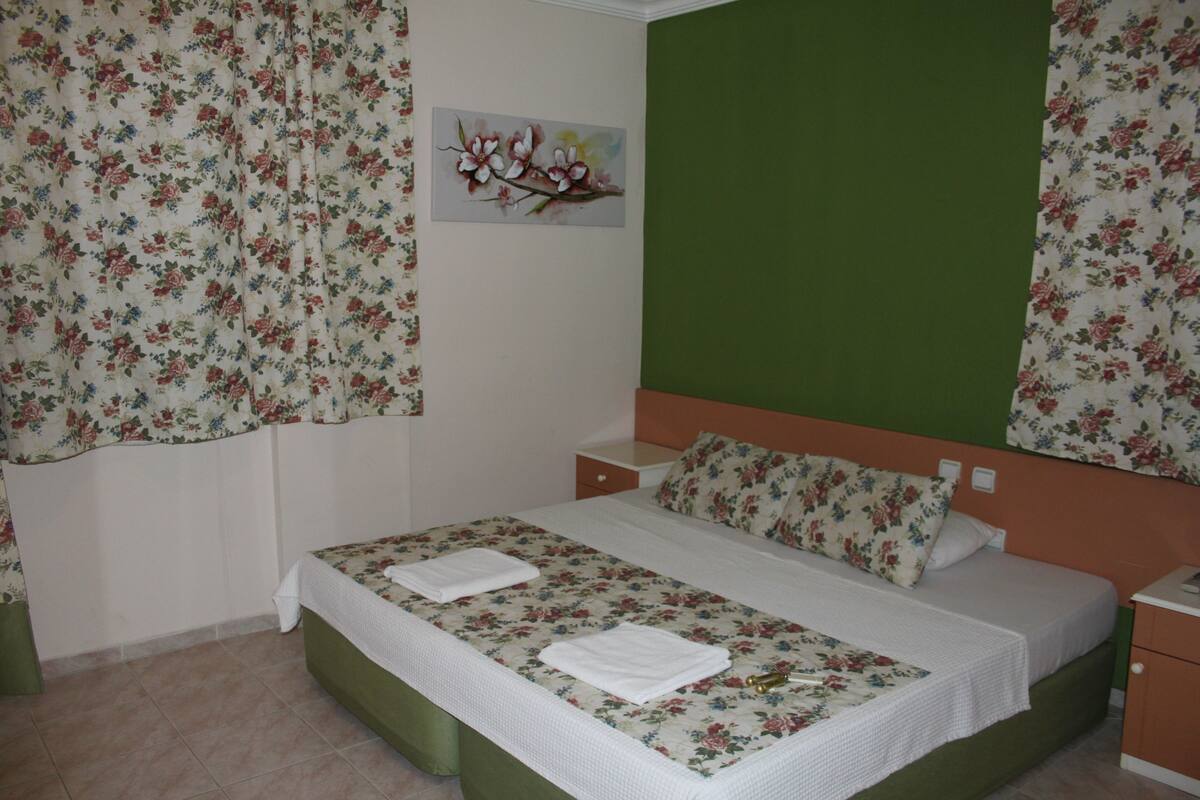 A bedroom with a floral bedspread, green headboard, and a painting on the wall.