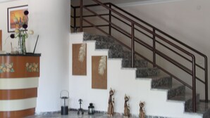 A staircase with a metal railing, a reception desk with a vase of flowers, and decorative wall art. - Villa Granada Hotel (Konyaalti)