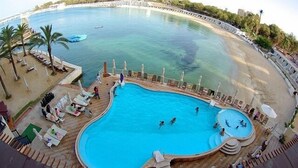 Ein großer, geschwungener Pool mit mehreren Ebenen und einer umlaufenden Sonnenterrasse mit Liegestühlen und Sonnenschirmen.