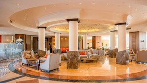 Eine großzügige Lobby mit gewölbter Decke, Marmorböden und mehreren Sitzbereichen mit modernen Möbeln.