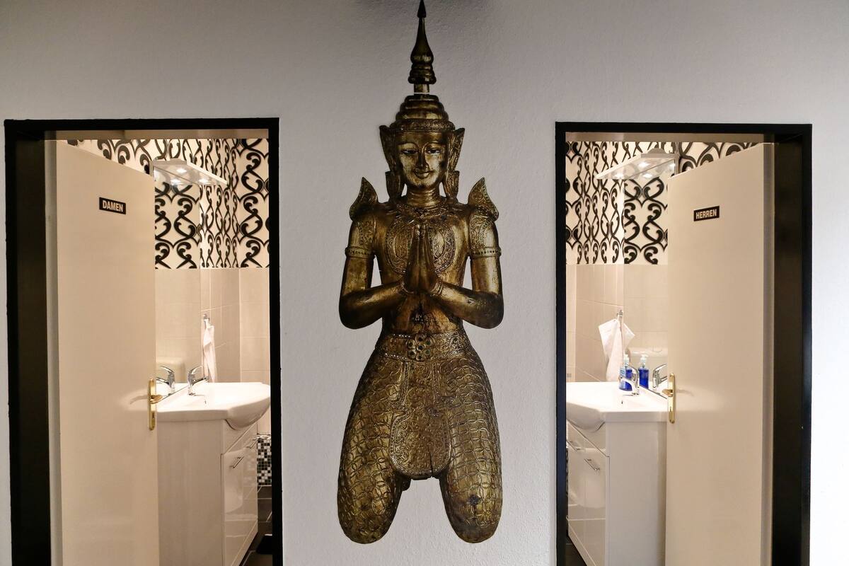 Une statue représentant une figure assise, placée dans une salle de bain équipée de deux lavabos et ornée de panneaux muraux décoratifs.