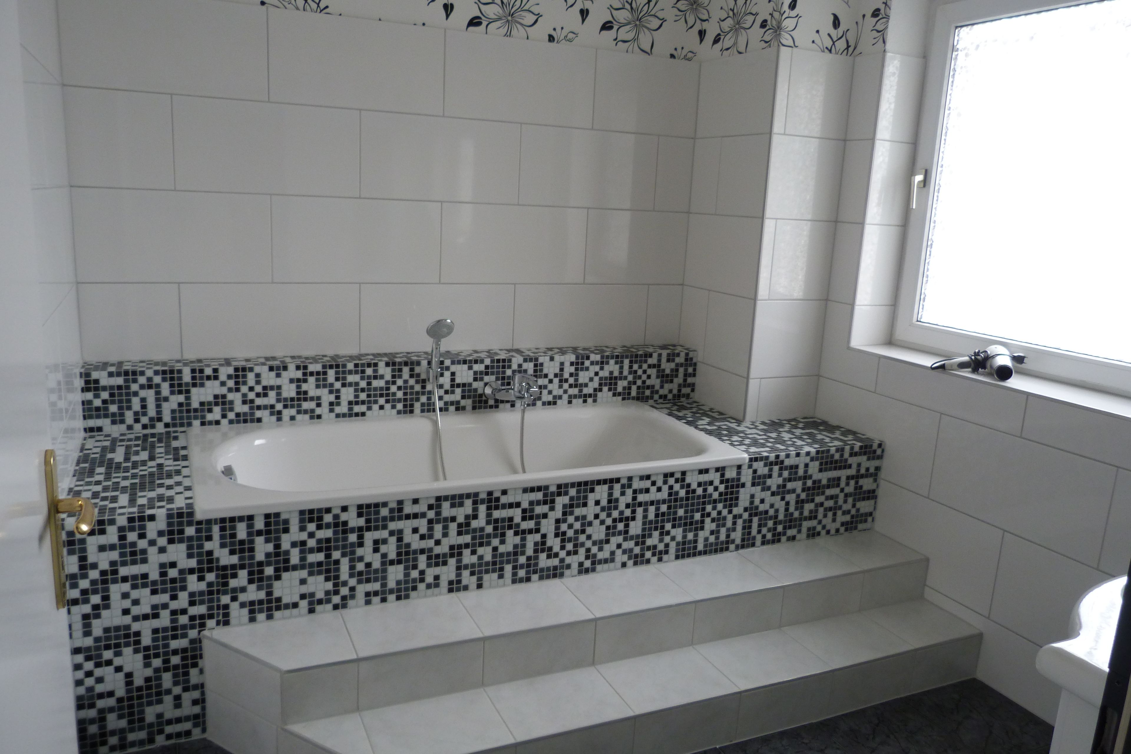 Une salle de bain avec une baignoire blanche, des murs carrelés et une fenêtre.