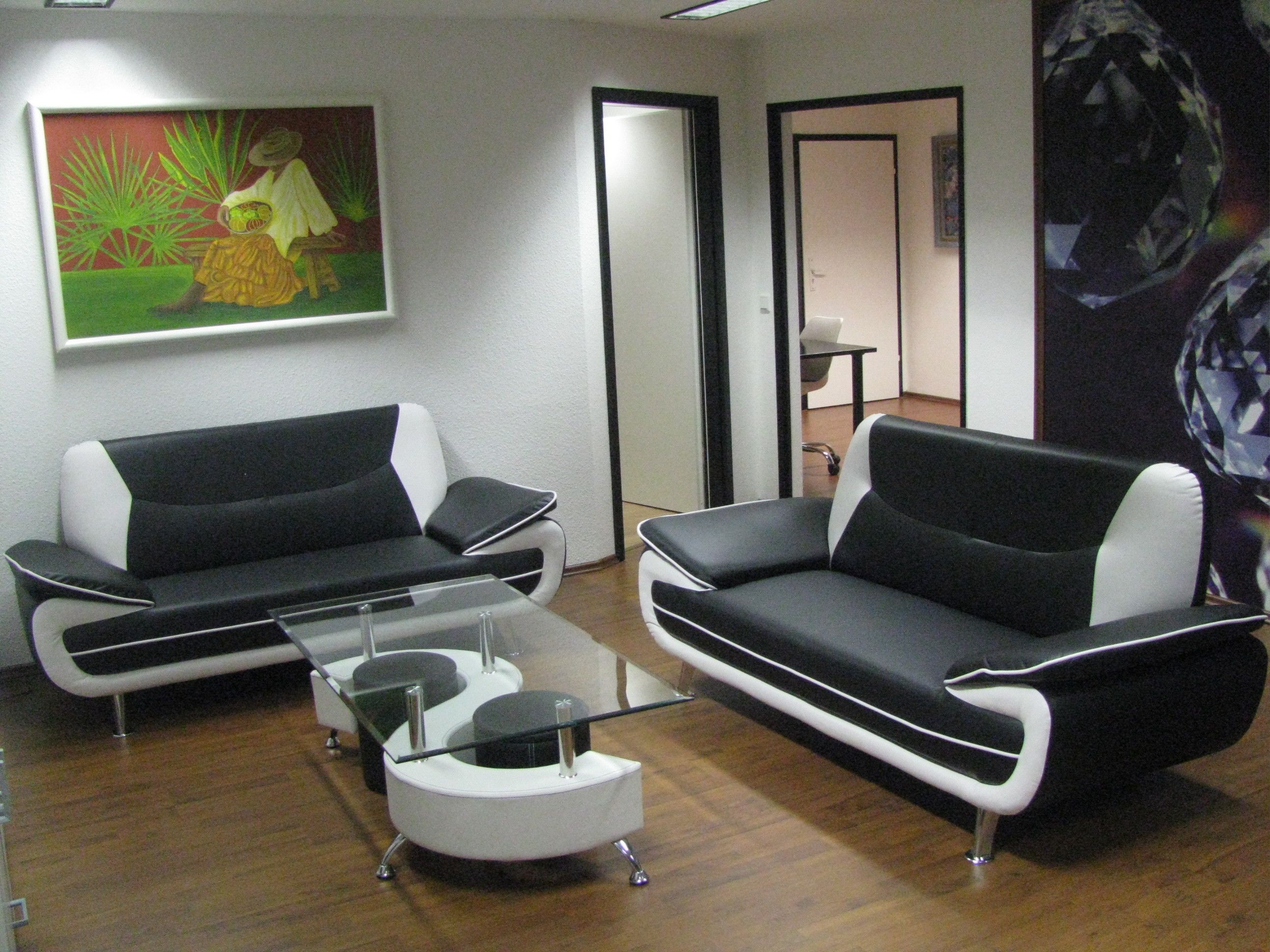 A modern living room with two black and white sofas, a glass coffee table, and a painting on the wall.
