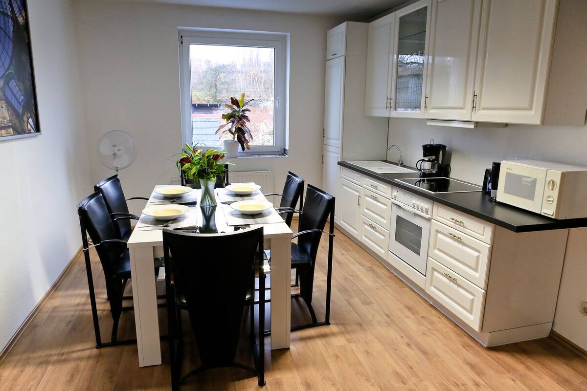 Une cuisine moderne avec des meubles blancs, un plan de travail noir et une table à manger pour quatre personnes.