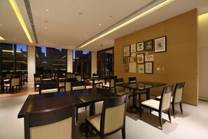 A modern dining area with tables and chairs, large windows, and framed artwork on the walls. - Aloft Dalian (Dalian)
