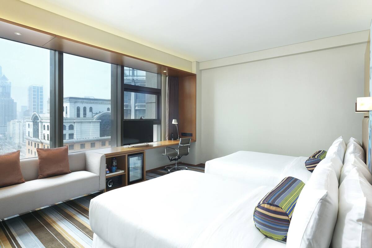 Ein Hotelzimmer mit großem Fenster, einem Bett, einem Schreibtisch und einer Couch.