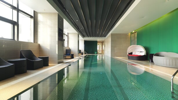 A modern indoor swimming pool with lounge chairs and a green wall. - Aloft Dalian (Dalian)
