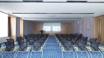 Un salón de conferencias con filas de sillas, un atril y un amplio ventanal.