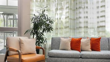 Una sala de estar con un sofá gris, cojines naranja, una silla de madera y una planta grande.