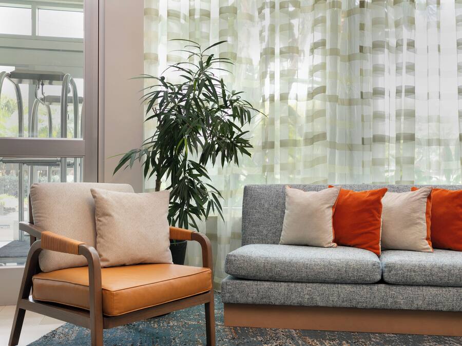 A living room with a grey sofa, orange cushions, a wooden chair, and a large plant.