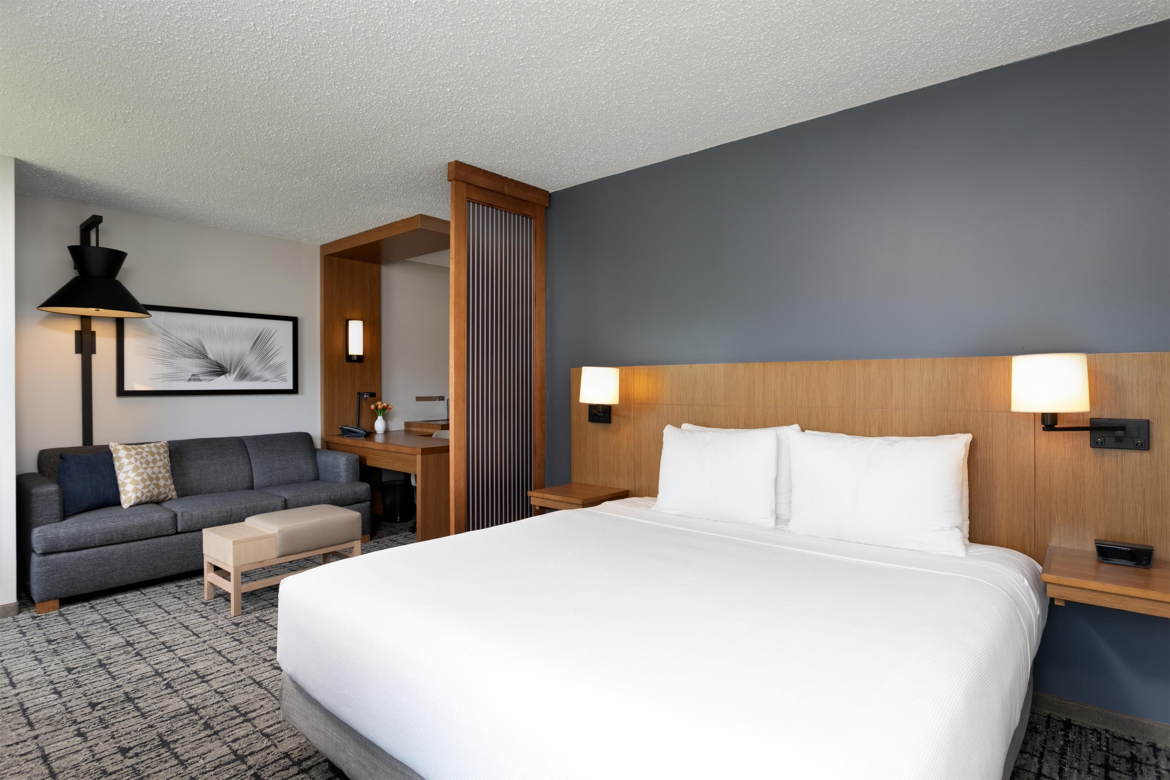 A hotel room with a large bed, a sofa, a desk, and a lamp.