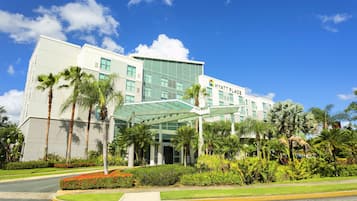 Een modern hotel met een glazen gevel, palmbomen en een helderblauwe lucht.