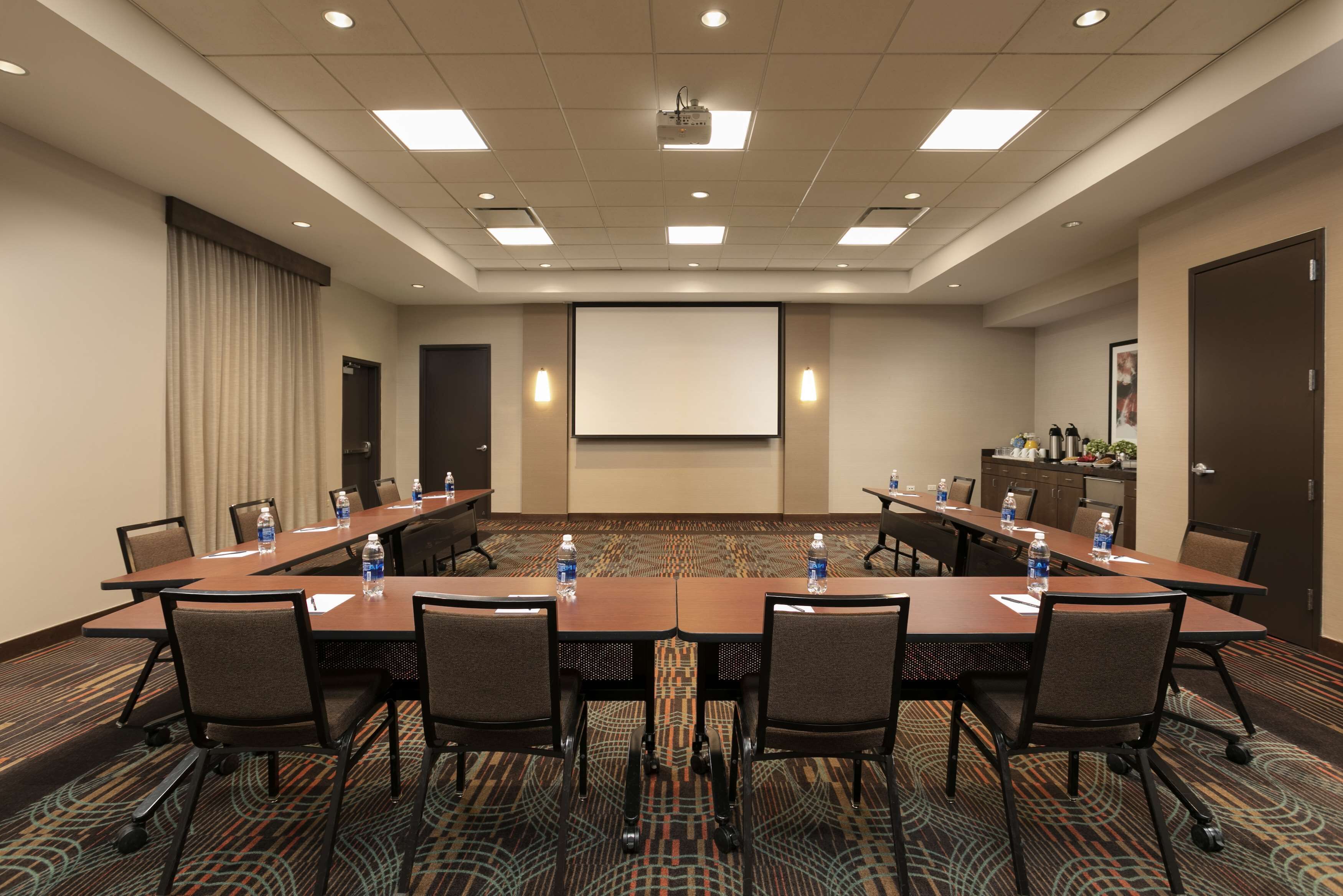 Une salle de conférence avec une longue table, des chaises, un écran de projection et un sol recouvert de moquette.