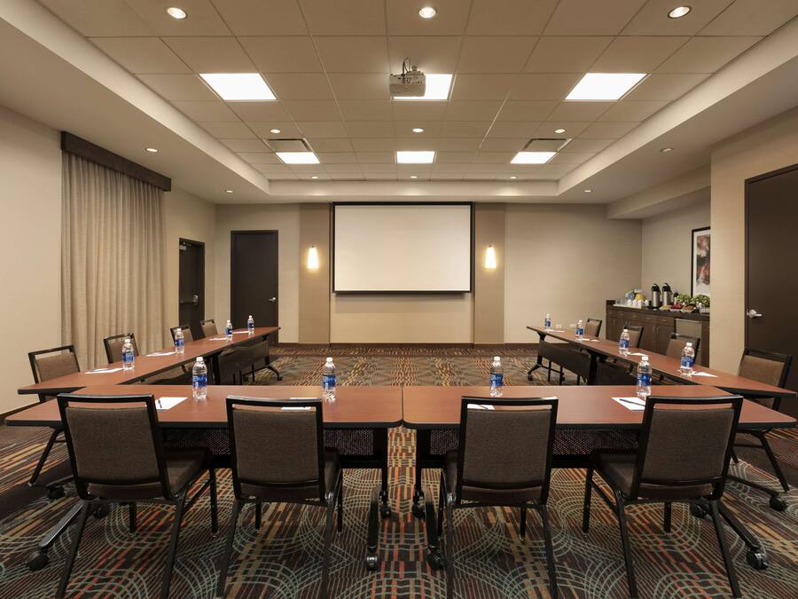 Une salle de conférence avec une longue table, des chaises, un écran de projection et un sol recouvert de moquette.