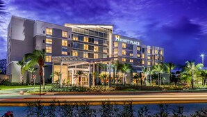 A modern hotel with a glass facade, a well-lit entrance, and a landscaped garden with palm trees. - Hyatt Place Manati (Manati)