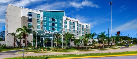 A modern hotel with a glass facade, palm trees, and a clear blue sky.