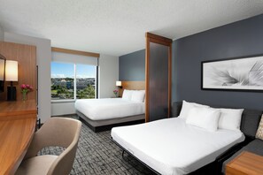 A hotel room with two beds, a desk, a chair, a large window with a city view, and a framed artwork on the wall. - Hyatt Place Manati (Manati)