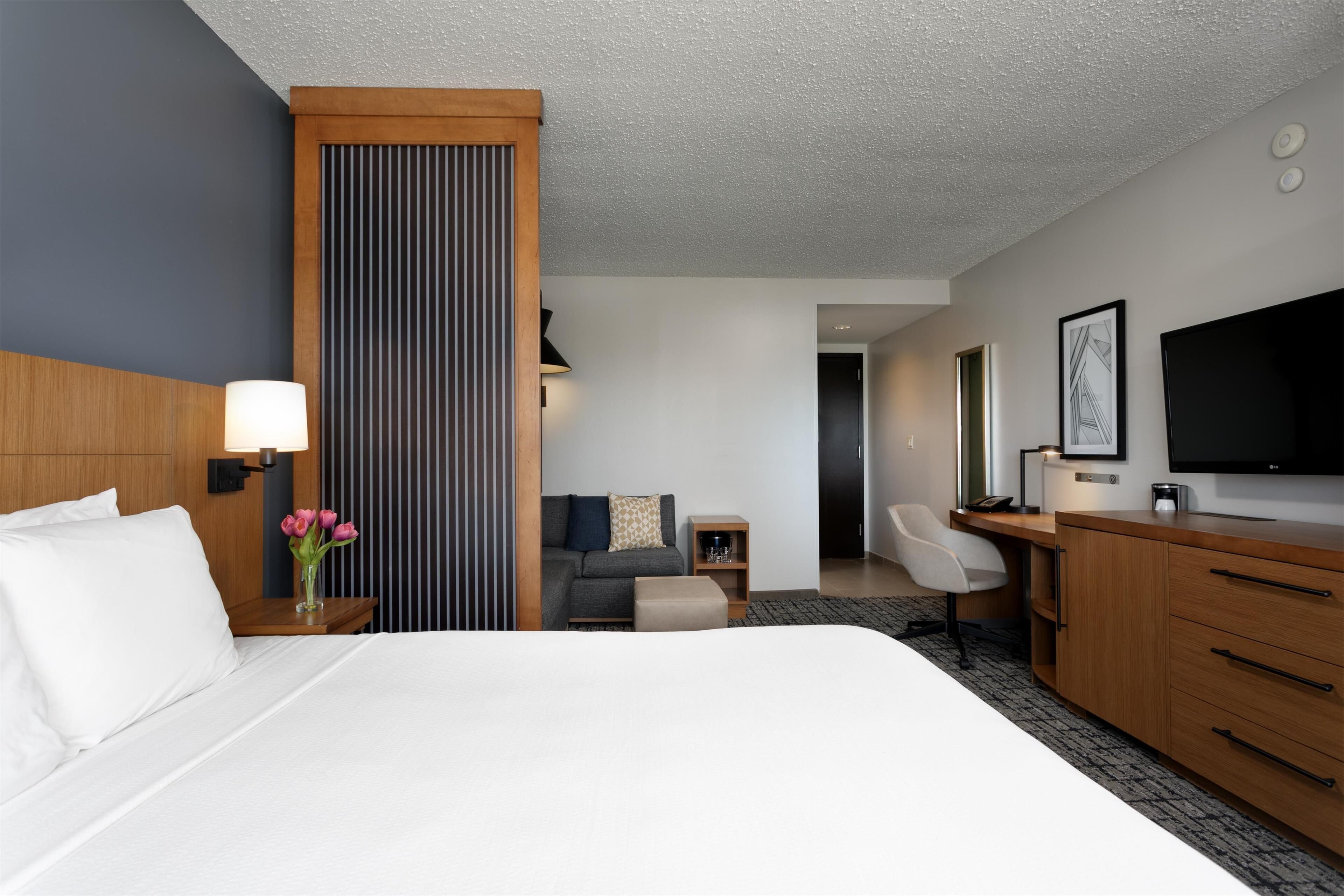 Une chambre d’hôtel avec un grand lit, un bureau doté d’un téléviseur à écran plat, un canapé et une armoire en bois.