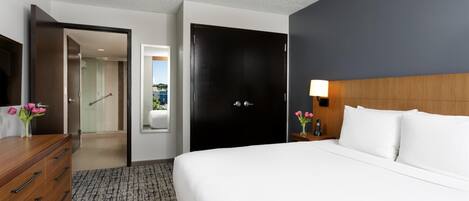 Habitación de hotel con cama, cómoda de madera, escritorio con lámpara y vistas al exterior.