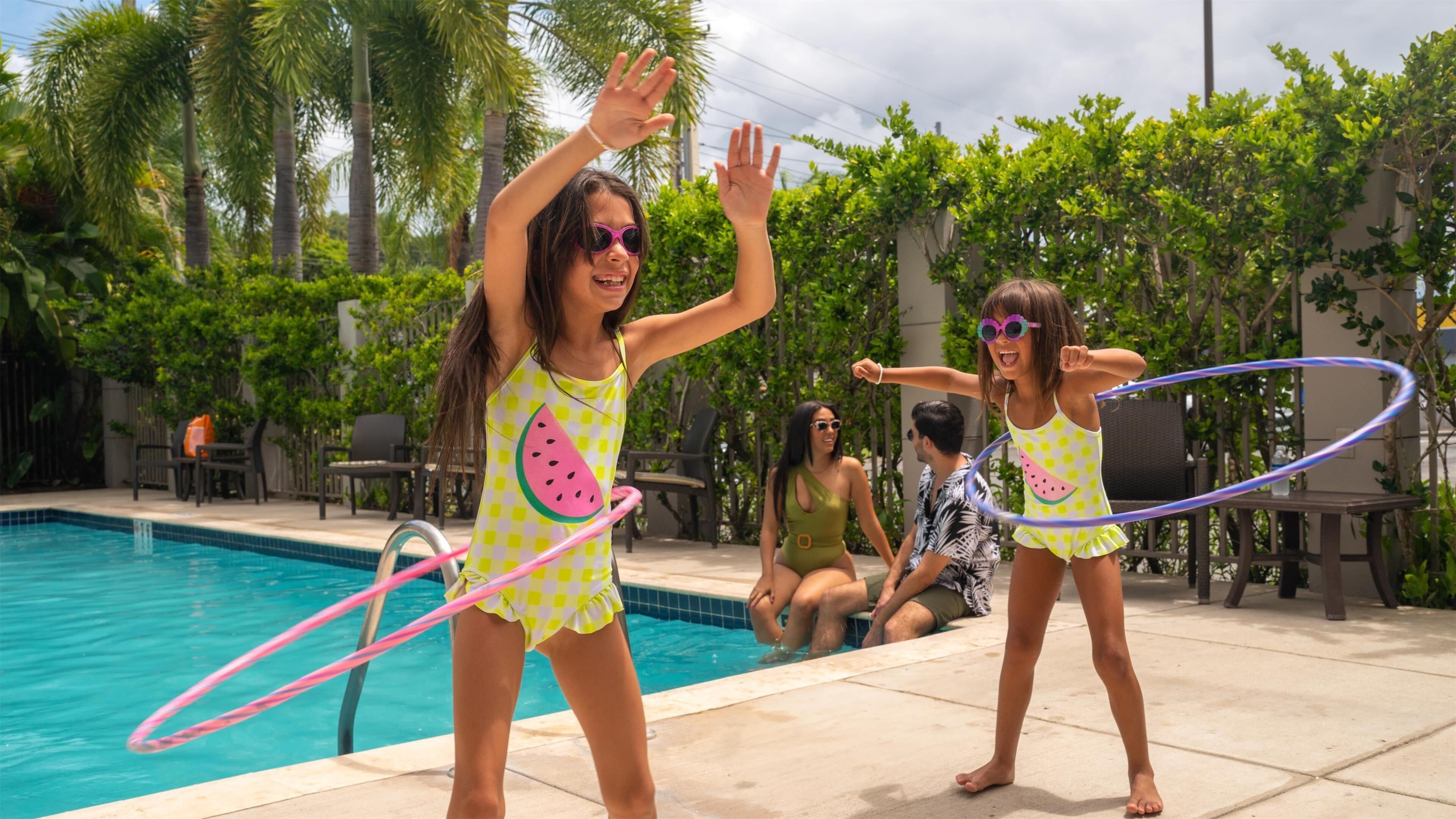 Two people playing with hula hoops by a poolside.