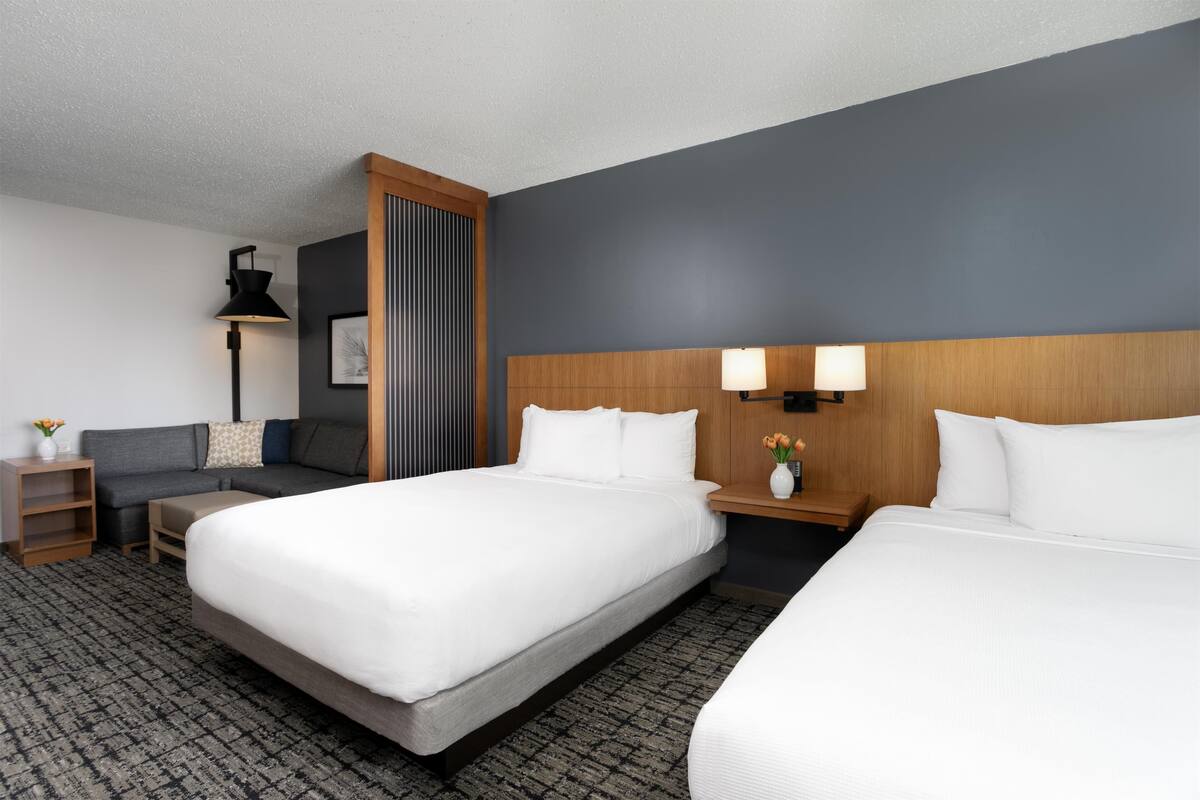 A hotel room with two beds, a sofa, a desk, and a lamp.