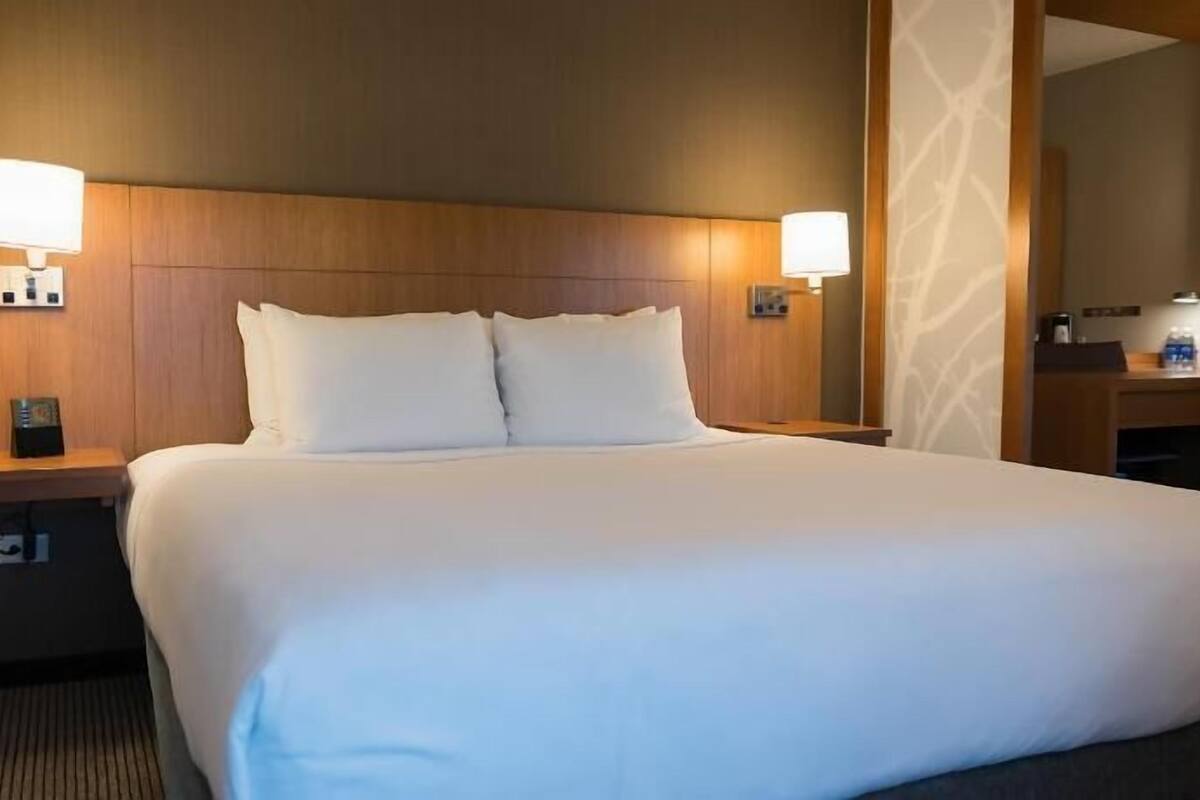 A hotel room with a large bed, two bedside tables with lamps, a mirror, and a small desk with a chair.