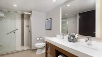 A modern bathroom with a glass shower enclosure, a white toilet, and a vanity with a large mirror.