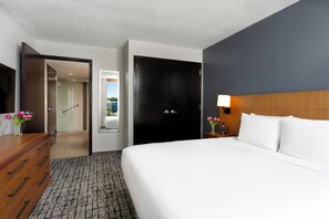 Une chambre d’hôtel comprenant un lit, une commode, un bureau, une lampe et une porte donnant accès à une salle de bain.