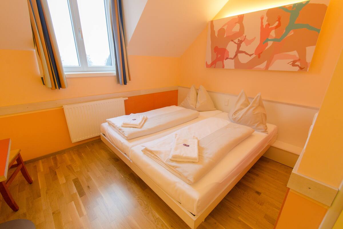Quarto com duas camas, um radiador, uma janela com cortinas e um quadro na parede.
