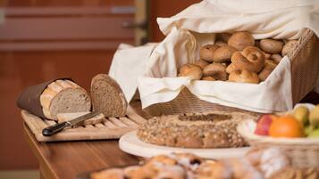 Variedad de panes y pasteles sobre una mesa de madera, incluyendo una hogaza, rebanadas de pan y una cesta de bollos redondos.