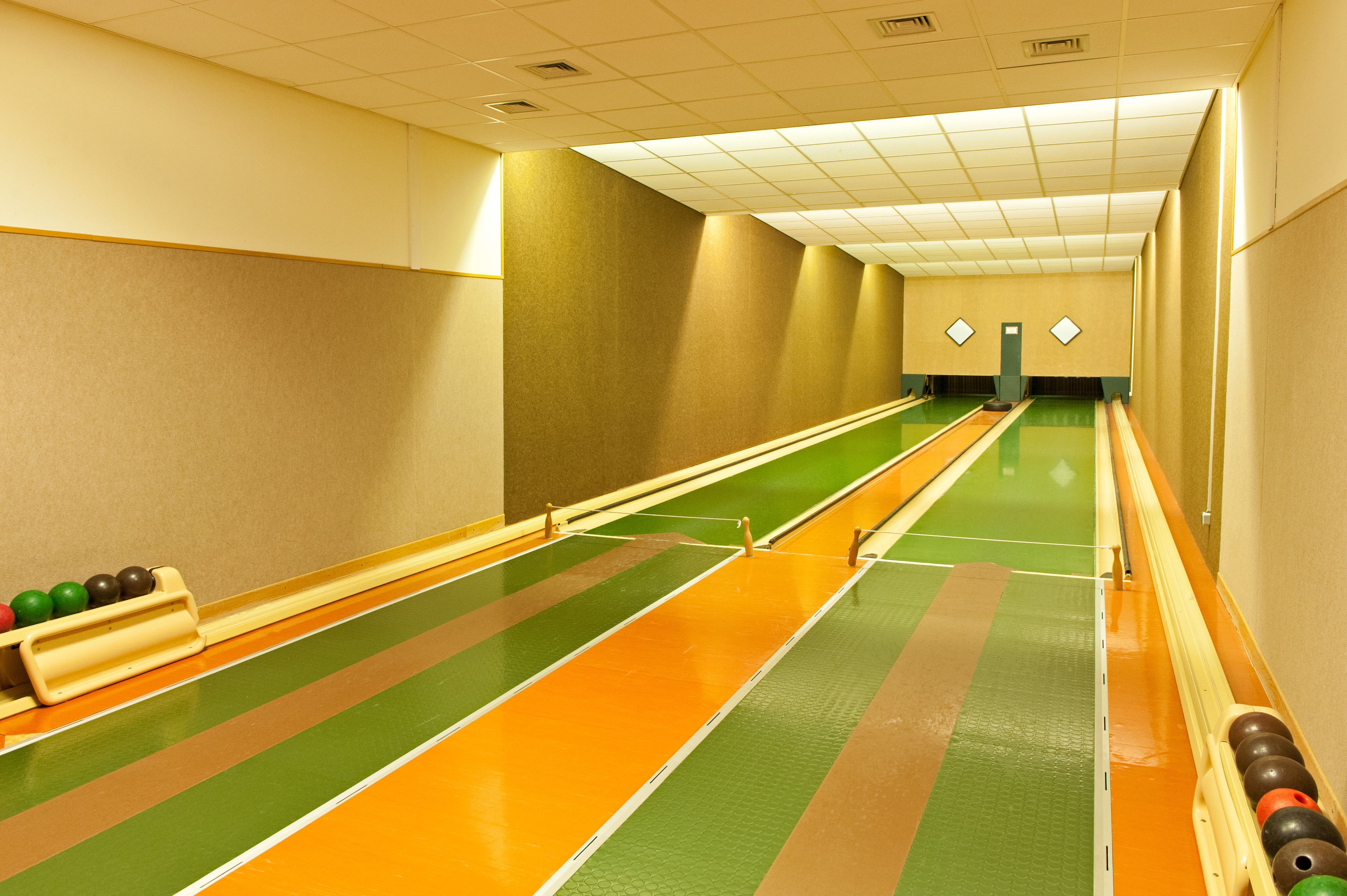 Een bowlingbaan met meerdere banen, groene en oranje markeringen en een vloer met groen tapijt.