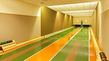 Een bowlingbaan met meerdere banen, groene en oranje markeringen en een vloer met groen tapijt.