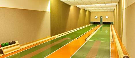 A bowling alley with multiple lanes, green and orange lane markings, and a green carpeted floor.