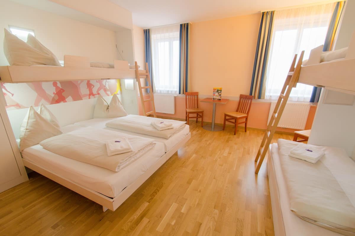 Quarto com duas camas beliche, uma mesa pequena com cadeiras e uma janela com cortinas.